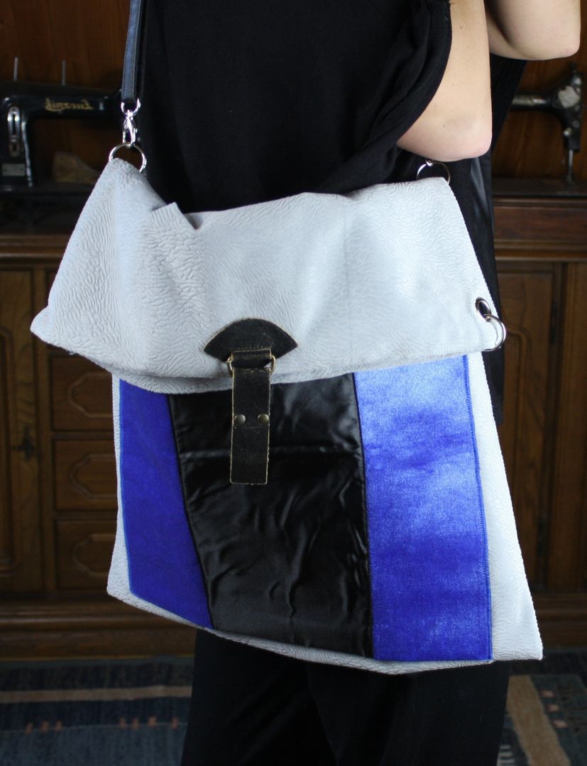 Szara torebka z weluru na ramię z atlasową kieszenią i skórzaną klamerką pokazana na ramieniu.