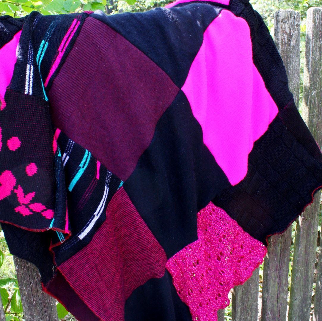 Wiszący na płocie kocyk zerowaste z różowo czarnych kawałków swetrów.